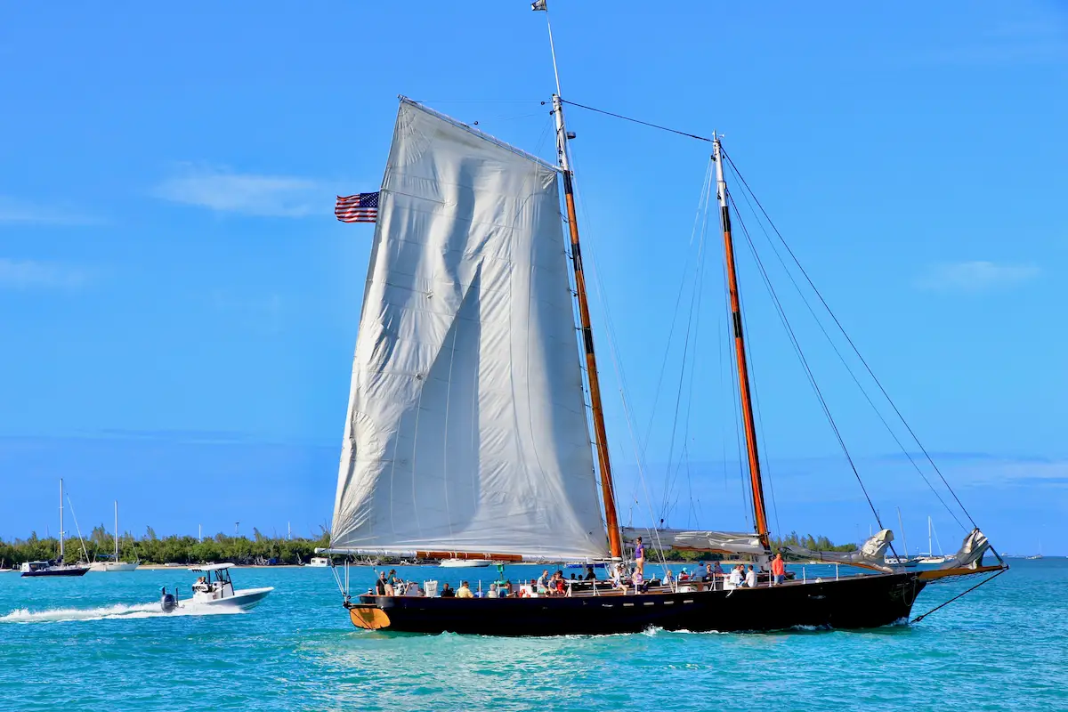 Schooner sailing off Key West with white sails, passengers on deck, turquoise water, and a small motorboat nearby