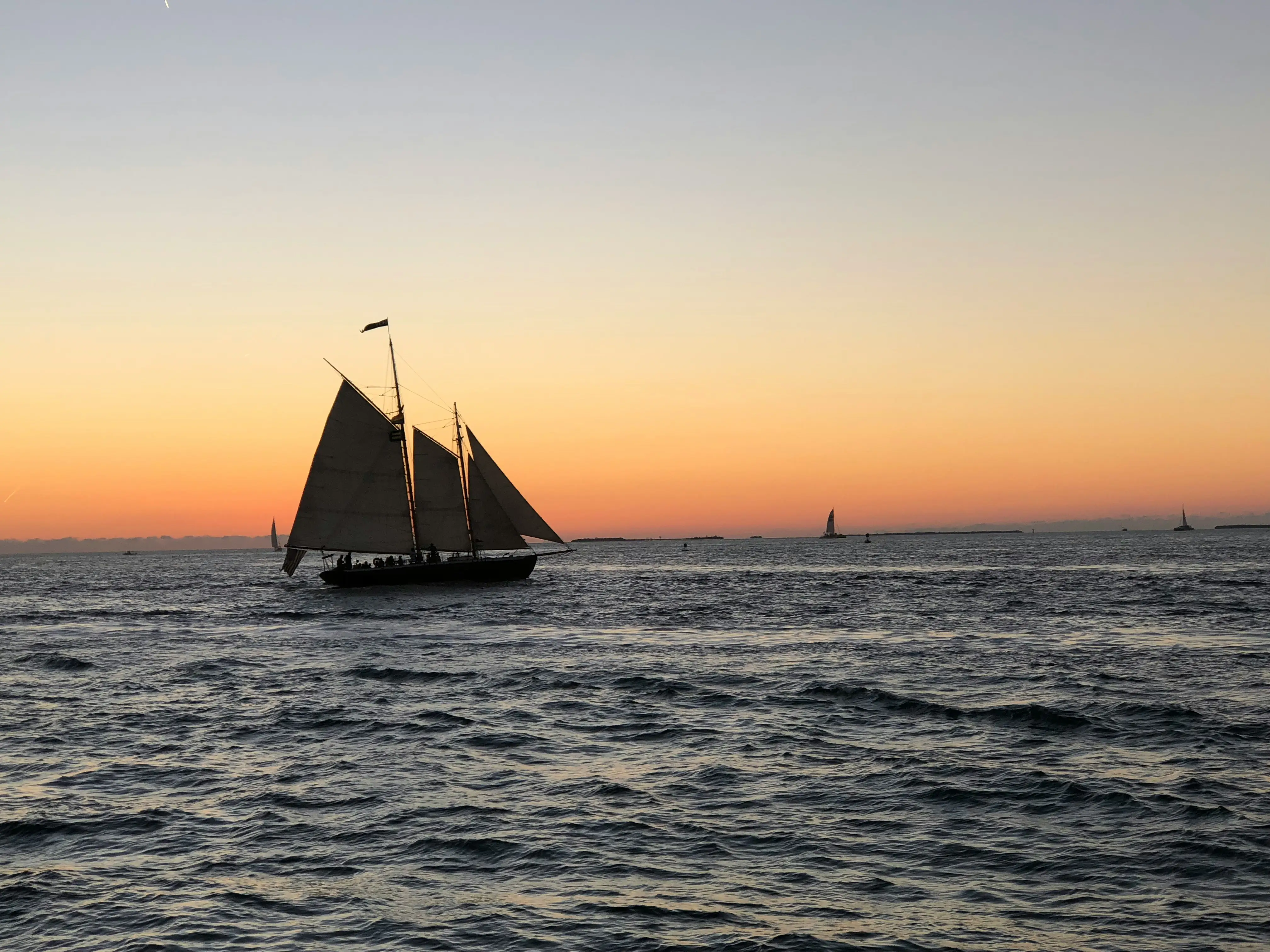 Sailboat on the water at sunset off Key West with orange sky and dark ocean waves